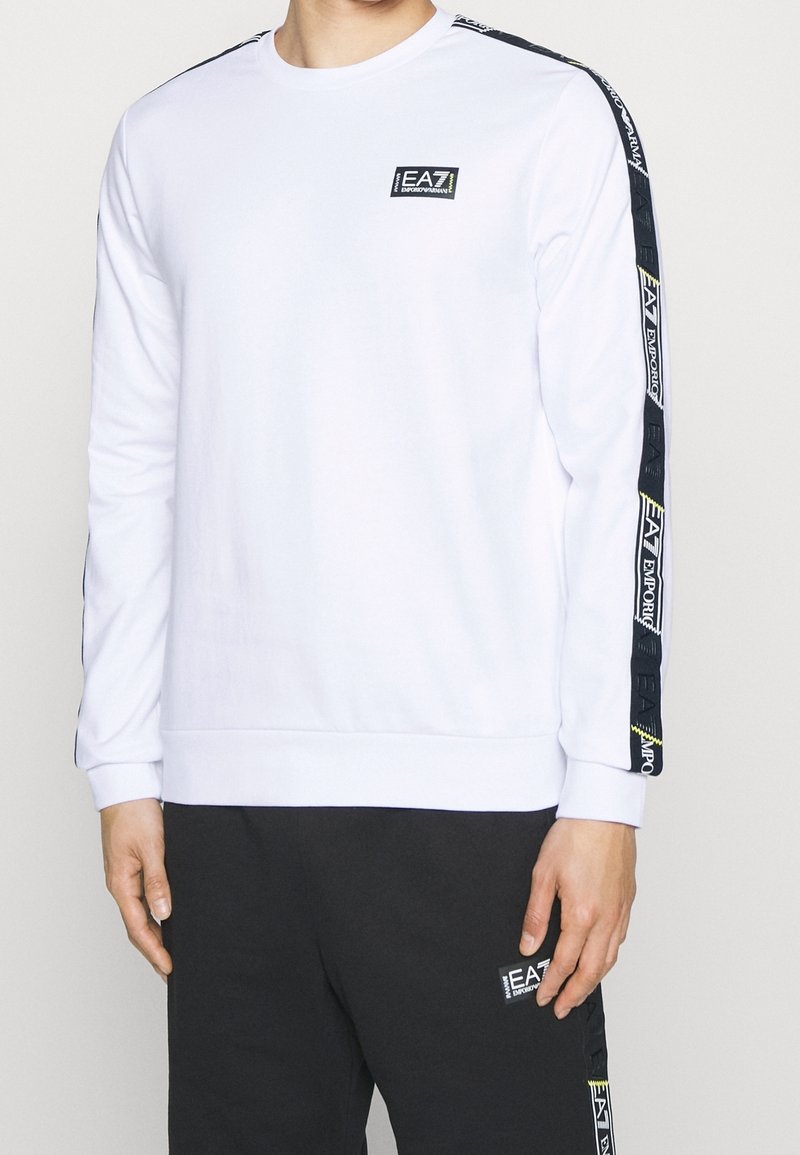 Vit långärmad sweatshirt med svart sidosträck som har logodetaljer. Ribbad mudd och nederkant, mjukt tyg, avslappnad passform.