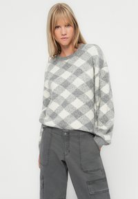 Grauer und weißer Pullover mit Diamantmuster aus weichem Stoff, mit rundem Halsausschnitt und lockeren Ärmeln, kombiniert mit grauen Cargo-Hosen.