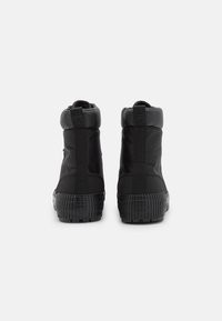 Baskets montantes noires avec une semelle en caoutchouc texturée, un talon renforcé, des panneaux latéraux élastiques et un col rembourré pour un meilleur maintien.