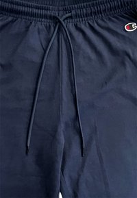 Pantaloni sportivi blu navy con vita elastica e cordoncino. Presentano una piccola etichetta del logo di lato. Texture liscia.