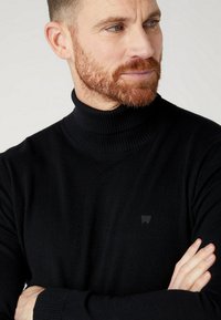 Czarny sweter z golfem wykonany z miękkiego materiału dzianinowego, z prążkowaną teksturą i subtelnym logo na piersi.