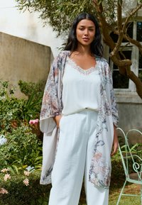 Lightweight floral kimono in soft pastel colors over a white lace-trimmed camisole and loose-fitting white pants, featuring side pockets.
