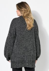 Svart och vit texturerad stickad cardigan med överdimensionerade ärmar, en lös passform och ribbad nederkant, sedd bakifrån.