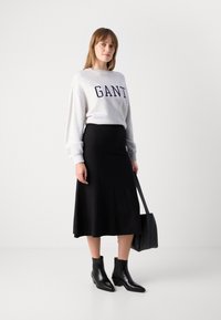 Grijze sweatshirt met "GANT" in marineblauw, gecombineerd met een strakke zwarte rok, zwarte enkellaarsjes en een zwarte handtas.