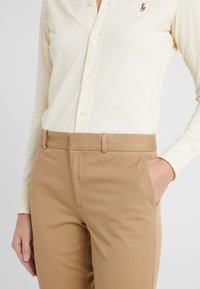 Světle žlutá košile s dlouhým rukávem, knoflíky a žebrovanou strukturou, doplněná béžovými kalhotami na míru s bočními kapsami a plochým předním dílem.