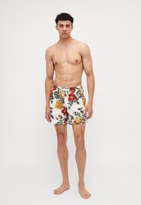 Costume da bagno floreale con sfondo bianco, caratterizzato da motivi floreali rossi, gialli e verdi, con cintura elastica e chiusura con lacci.