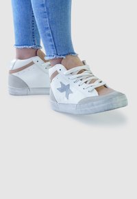 White and beige sneakers with a grey star logo, featuring soft suede accents and white laces, paired with blue denim jeans.