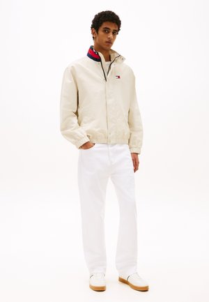 Beige lightweight jacket with a colorful collar, paired with white straight-leg jeans and white sneakers with a tan sole.