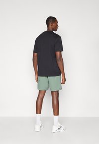 T-shirt noir à manches courtes associé à un short vert clair. Le modèle porte des chaussures de sport blanches et des chaussettes blanches de longueur moyenne. Design et coupe simples.