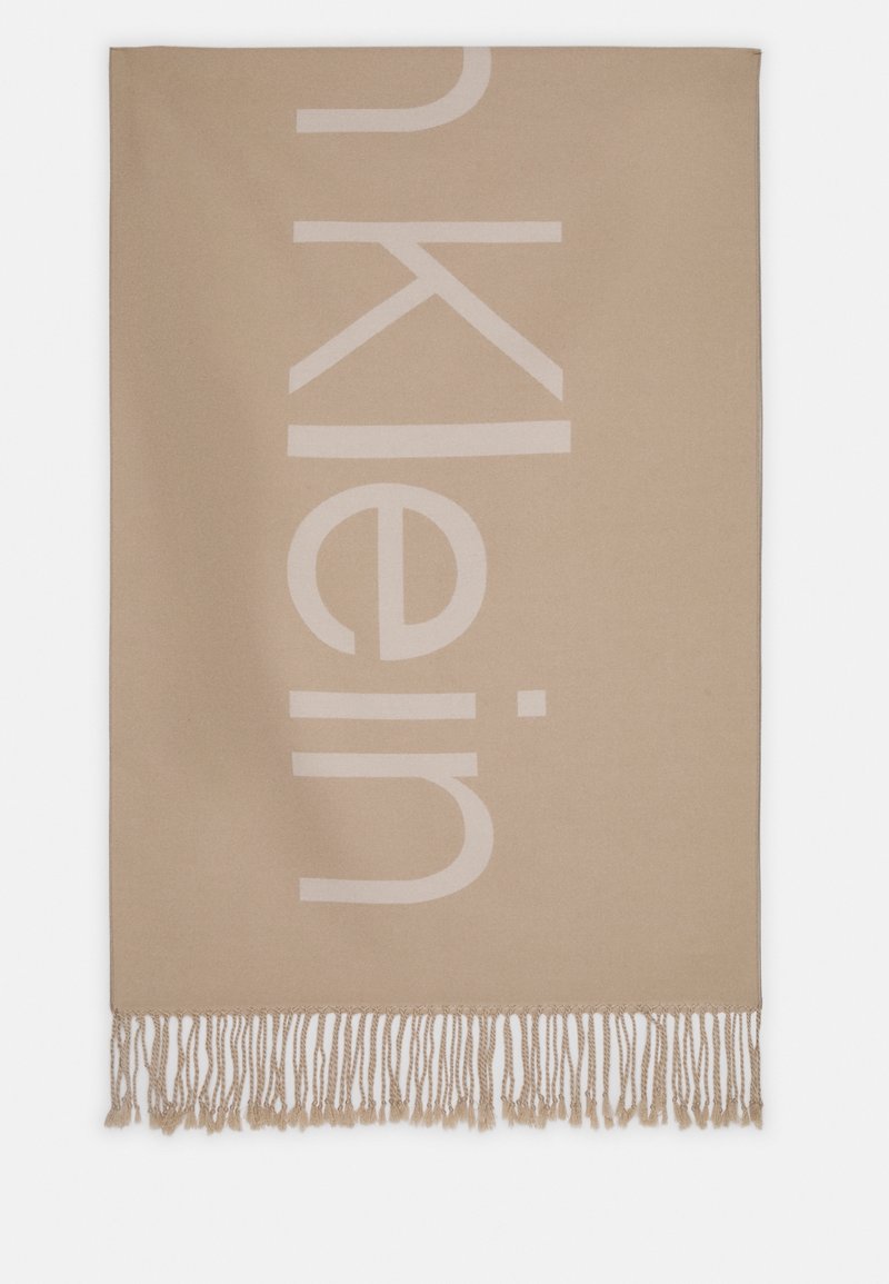 Écharpe beige avec des franges beige clair et de grandes lettres verticales formant partiellement "Calvin", partiellement visibles.