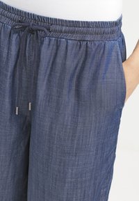 Modré lněné kalhoty s elastickým pasem, stahovací šňůrkou a bočními kapsami. Tkanina má hladkou, lehkou texturu.