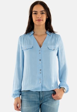 Blusa azzurra a maniche lunghe con scollo a V, due tasche sul petto, bottoni in argento sulla parte frontale e polsini arricciati. Texture satinata.
