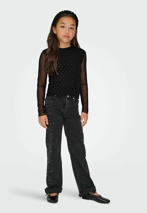 Czarna bluzka z długim rękawem, wykonana z przeźroczystego, kropkowanego materiału; w komplecie z czarnymi dżinsami z rozrzuconymi ozdobami oraz czarnymi balerinami.