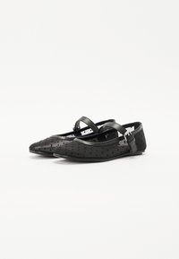Black ballet flats with a rounded toe and transparent polka dot fabric. Features a thin strap with a metallic buckle and flat sole.