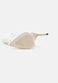 Chaussure blanche à talon haut avec une semelle texturée et une forme angulaire. Présente une tige lisse et un bout étroit et pointu avec un accent noir.