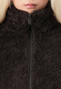 Svart fleece zip-up jacka med hög krage, med en mjuk, texturerad yta och en central svart dragkedja.