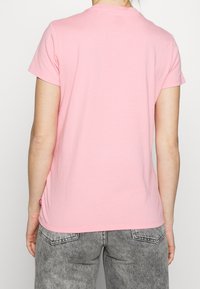 Růžové bavlněné tričko s krátkým rukávem, kulatým výstřihem a volným střihem. Obsahuje malou logo etiketu po straně.