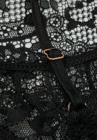 Schwarzer Spitzenstoff mit Blumenmustern und einem schwarzen verstellbaren Riemen mit einer kleinen goldenen Schnalle.