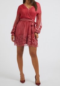 Robe rouge à manches longues semi-transparentes, en tissu texturé, avec des broderies florales sur l'ourlet. Comprend une ceinture assortie pour définir la silhouette.