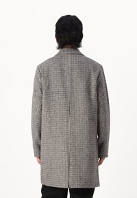 Abrigo largo a cuadros con un patrón en gris y negro. Cuenta con cuello, corte recto y mangas largas; está hecho de un tejido texturizado.