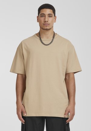 Beige oversized t-shirt van katoen met een ronde hals. Korte mouwen en een rechte zoom. Draag een zwarte ketting als accessoire.