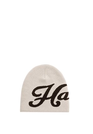 Gorro de punto beige claro con grandes letras cursivas negras parcialmente visibles en el frente.