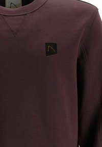 Sweatshirt bordeaux con collo a giro e orlo a coste, dotato di una piccola etichetta nera con logo arancione sul lato sinistro del petto. Consistenza morbida.