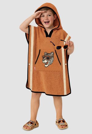 Smilende barn iført en brun hættehåndklædeponcho med et tigerdesign iført solbriller, der holder matchende solbriller og har tiger-hjemmesko på.