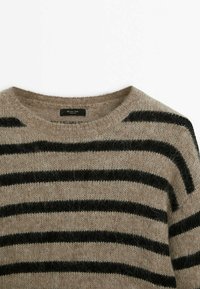 Beżowy sweter dziany z szerokimi czarnymi poziomymi paskami, okrągłym dekoltem, miękką teksturą i widoczną metką. Casualowy design.