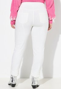 Witte, aansluitende broek met een gladde textuur, voorzien van twee achterzakken. Gecombineerd met zilveren enkellaarsjes voor een contrasterende uitstraling.