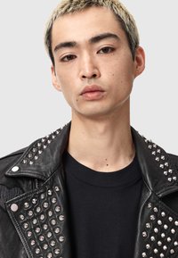 Jachetă de motociclist din piele neagră cu ținte argintii pe umeri, asortată cu un tricou negru simplu. Textură netedă și design structurat.