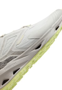 Chaussure de sport blanche et gris clair avec semelle texturée vert citron vert et trous de ventilation le long du côté de la semelle intermédiaire.