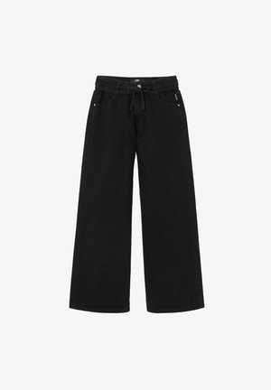 Chemise noire courte à boutons, pantalon noir large, chaussures marron et bonnet côtelé vert avec détail de logo.