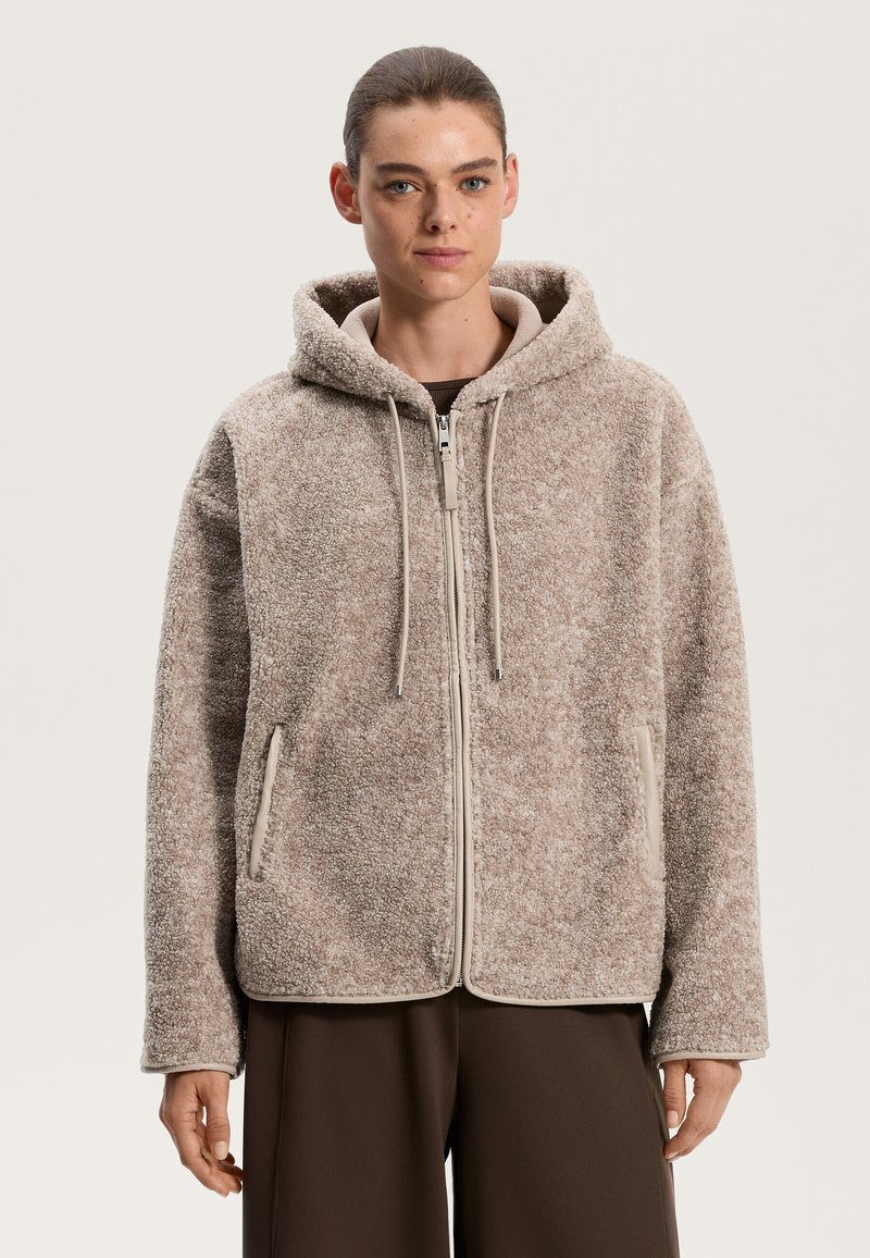 Felpa marrone con zip, cappuccio, tasche frontali e coulisse. Tessuto texture con bordi e dettagli beige a contrasto.