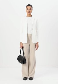 Hvit skreddersydd blazer over en hvit topp, kombinert med beige vide bukser. Svart håndveske og sko. Enkle, rene linjer.