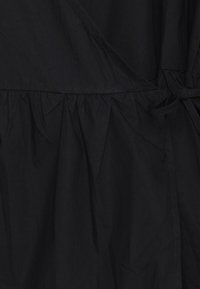 Gros plan sur un tissu noir avec une section froncée et un détail de nœud noué, montrant la texture et les coutures d'un vêtement.