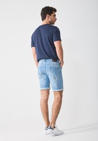 Navy t-shirt, light blue denim shorts with cuffed hems, and white sneakers. Features a brown leather patch on the waistband.