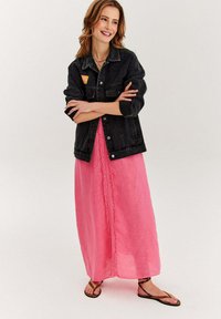 Czarna denimowa kurtka na różowej lnianej sukience maxi z koronkowym wykończeniem, w zestawie z brązowymi sandałami na ramiączkach na jasnym tle.