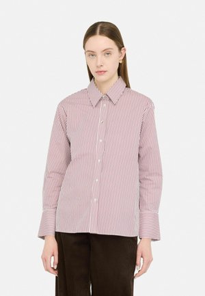 Camicia bianca con sottili righe rosse, maniche lunghe e colletto classico; presenta bottoni sulla parte anteriore e polsini svasati.