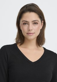 Pull noir à col en V avec une texture côtelée et des manches longues. Design simple, près du corps, fabriqué dans un tissu léger.
