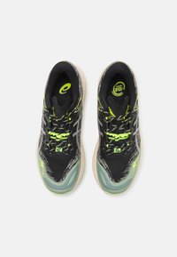 Baskets de sport noires avec des accents gris et des détails en vert fluo. Tige texturée, semelle amortissante et logo réfléchissant sur la languette.