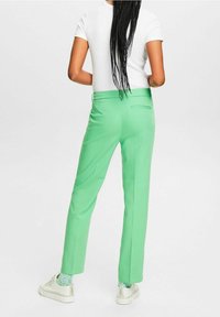Green tailored trousers with a smooth texture, slim fit, and back pocket detail, paired with a white fitted shirt and sneakers.