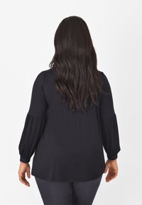 Czarna bluzka z długim rękawem o luźnym kroju, z bufiastymi rękawami i miękką, gładką teksturą. Tło jest jednolite, białe.