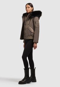 Ruskea toppatakki, jossa musta karvahuppu, sivutasku vetoketjulla ja resorireunus. Yhdistetty mustien legginsien ja massiivisten mustien saappaiden kanssa.