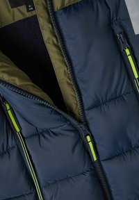 Doudoune marine avec doublure intérieure olive, équipée de deux zips avant noirs avec des accents vert fluo et une surface texturée matelassée.