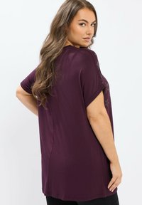Fioletowa bluzka z krótkim rękawem o luźnym kroju, z miękką teksturą i sitodrukiem srebrnej gwiazdki na ramieniu. Czysta sylwetka, klasyczny styl.
