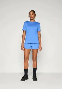 Gaiši zils sporta divdaļīgais tērps, kas sastāv no īsām piedurknēm un šortiem, izgatavots no gludas auduma, kombinēts ar melnām kurpēm un zeķēm.