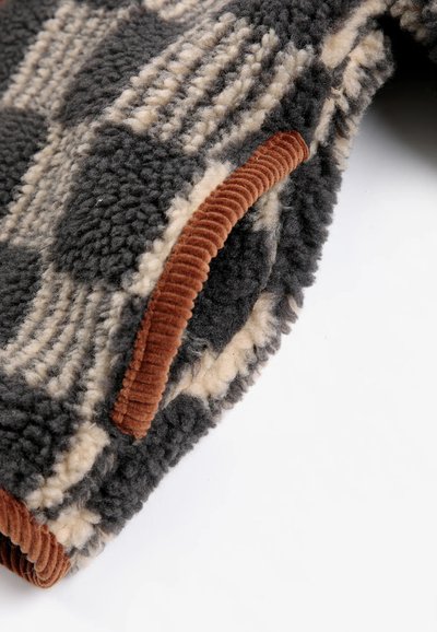 Gros plan d'un tissu polaire doux à motif à carreaux noir et beige avec une bordure en velours côtelé marron.