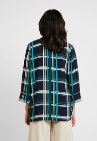 Námořnická modrá volná košile s kostkovaným vzorem v zelené a bílé barvě, tříčtvrteční rukávy a rovný spodní lem, vyrobená z jemné látky.