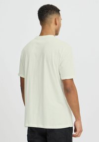 Camiseta de algodón color beige claro con cuello redondo, mangas cortas y puños enrollados, presenta una textura lisa y un corte holgado.